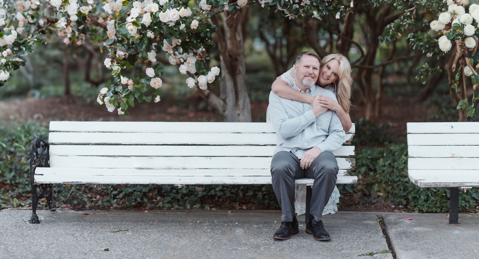 Couple sitting together on a white park bench under blooming trees