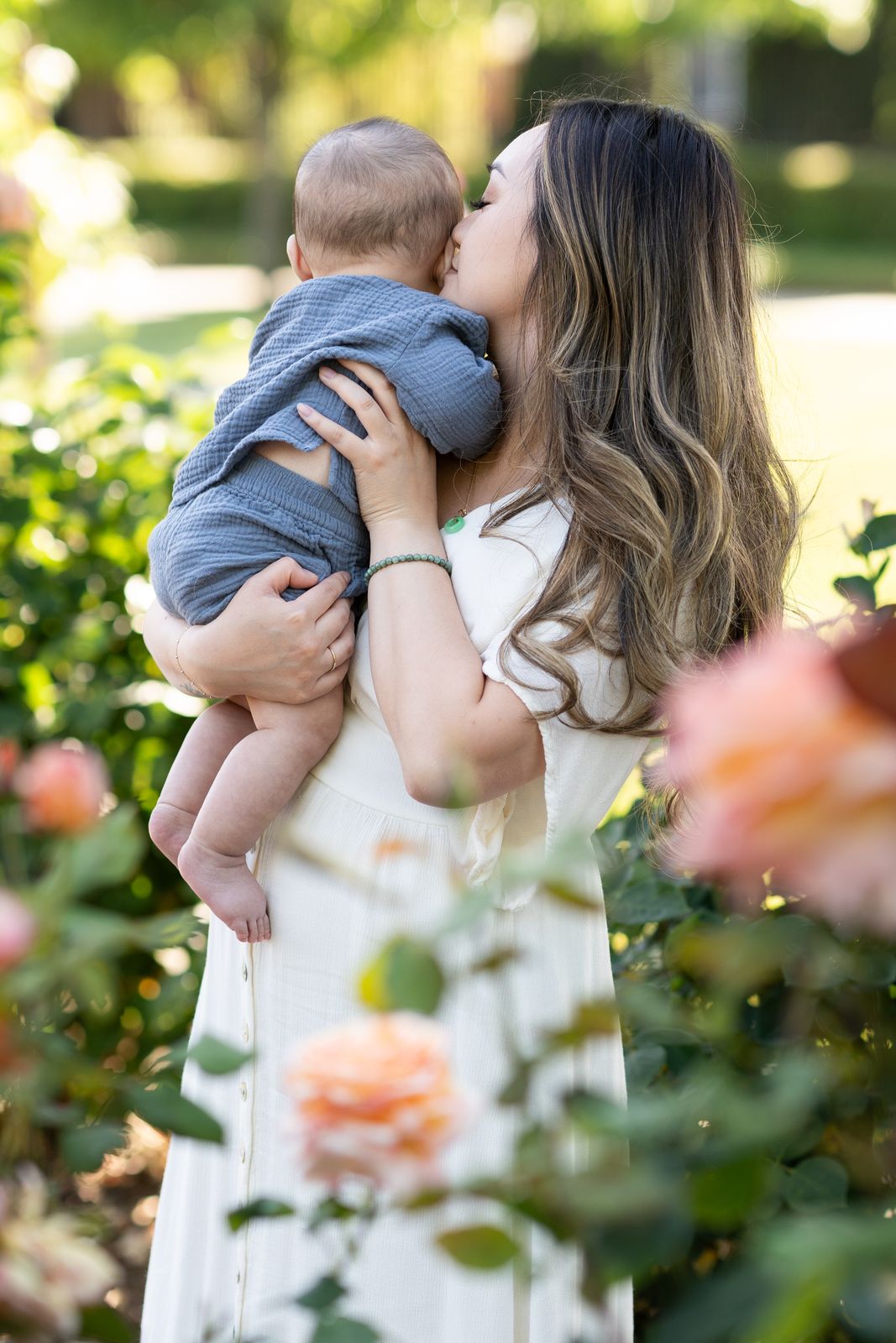 Mother kissing her baby among pink roses