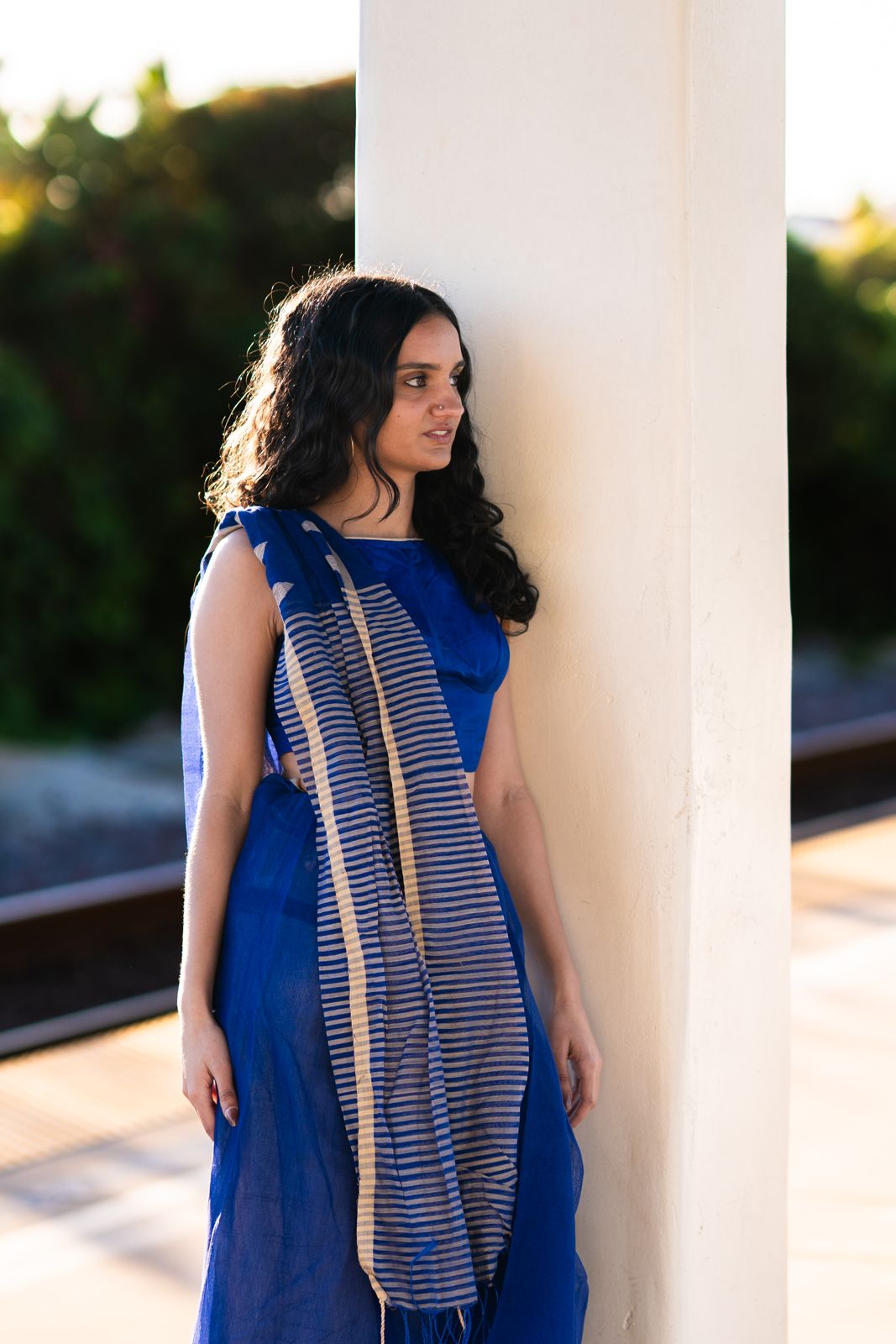 Woman in a royal blue saree leaning on a pillar and looking away
