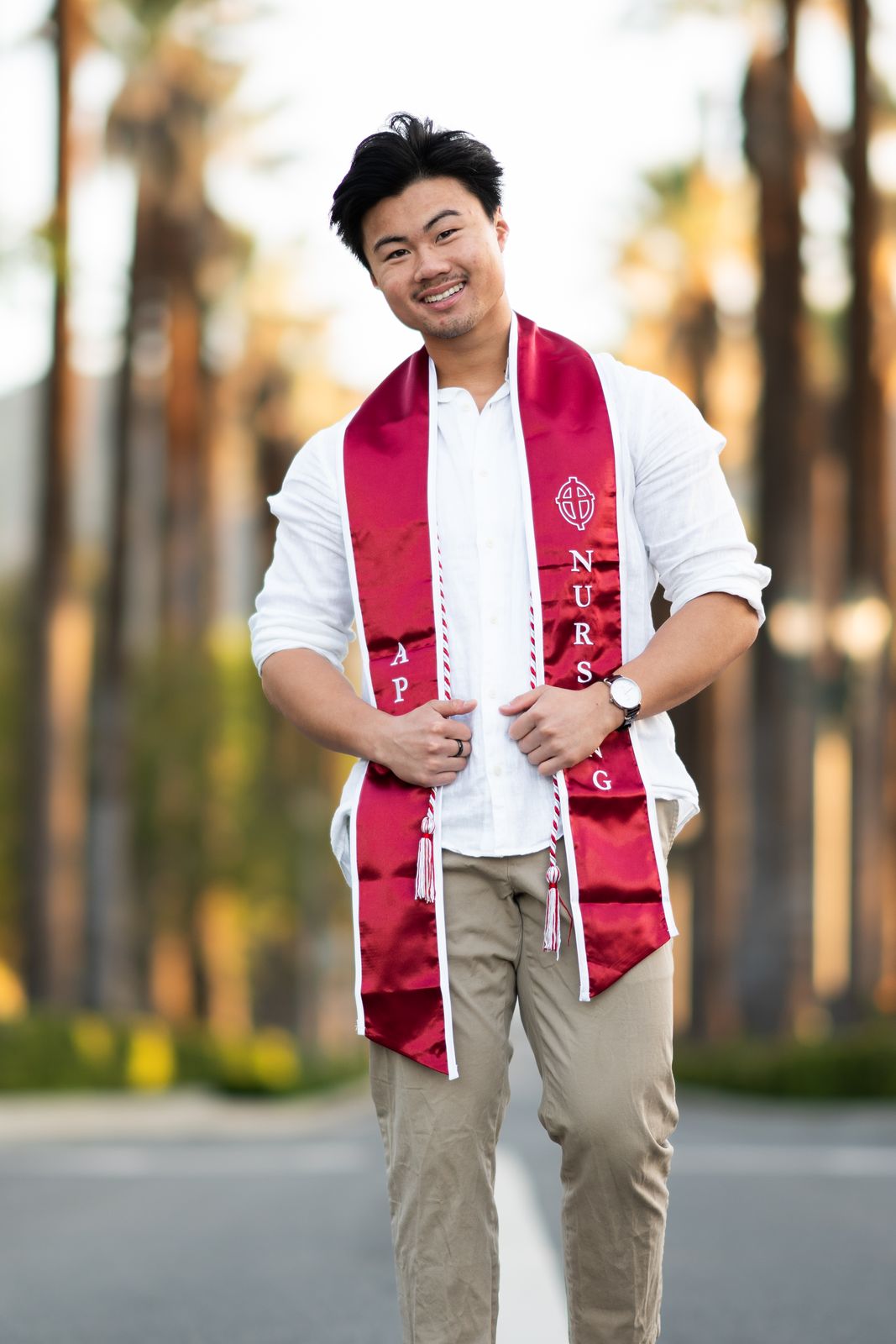 Nursing graduate in a red stole on a palm-lined street