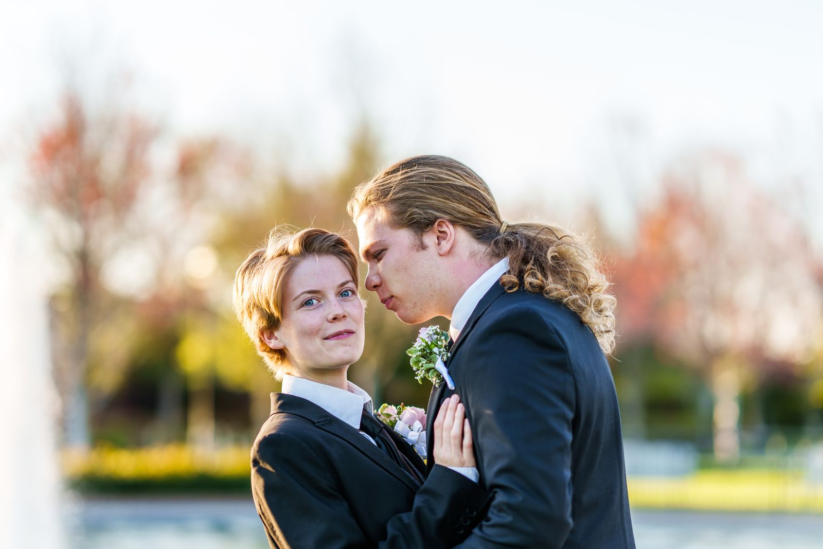 Couple in suits posing by a lake in autumn light